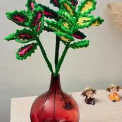 A fuller arrangement of my crochet coleus plants, with vibrant green, pink, and yellow leaves, displayed in a dark red vase.