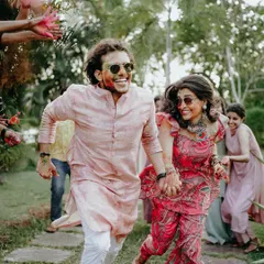 The pure energy of a Haldi celebration. Amal and Anju run hand-in-hand, their faces smeared with color, surrounded by the happy chaos of their friends and family.