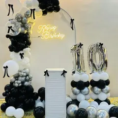 A chic black, white, and silver theme for a 10th birthday, featuring a minimalist arch, a neon sign, and balloon columns with foil numbers.