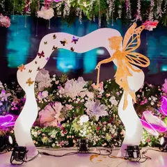 A stunning entrance arch for an enchanted garden party. A custom-sculpted fairy and butterfly archway welcomes guests into a world of magic, set against a backdrop of lush flowers and glowing butterflies.