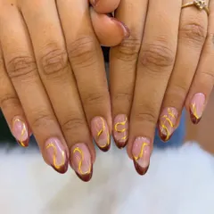 An earthy and elegant version of the French manicure, featuring deep brown tips and abstract golden swirls over a nude base.