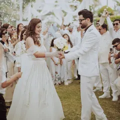 The couple makes their grand entrance, surrounded by cheering family and friends. This candid shot captures the excitement and celebratory atmosphere of their all-white themed event.