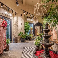 The view from the entrance captures the key elements of our design: the central water feature, lush indoor plants, and racks of vibrant designer clothing. The black and white chevron floor tiles add a graphic, modern contrast to the vintage decor.