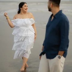 A candid moment of a woman walking on the beach in a beautiful white dress, with her partner looking on. This shot from their Alibaug pre-wedding session captures a sense of freedom and natural interaction.