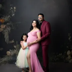 An elegant family maternity portrait against a moody, dark backdrop. The family's coordinated outfits in shades of pink and burgundy create a sophisticated and cohesive look.