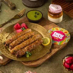 Juicy Seekh Kebabs fresh off the grill for Chew Chapad. The lighting highlights the smoky char and texture, while the mint and pickled onions suggest the fresh accompaniments that complete the dish.