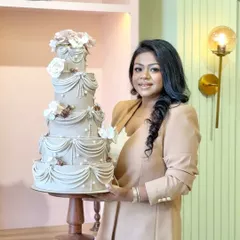 This is more than a cake; it's a canvas for your celebration. Here I am in our new studio with an elegant, multi-tiered wedding cake featuring intricate drapery and sugar flowers, a testament to the artistry we pour into every creation.
