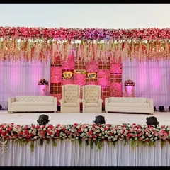 This reception stage is a vision in pink, featuring a ceiling of hanging floral strings and a dense flower border. The combination of plush white seating and warm pink lighting creates a romantic and luxurious atmosphere.