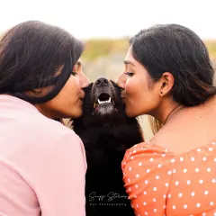 Two women share a kiss with their happy black dog, a perfect picture of a family full of love.