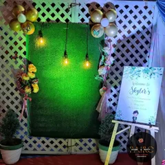 For a more modern and rustic theme, I created this backdrop using a green turf wall and a white lattice panel. The setup is completed with a personalized welcome easel, balloons, and warm Edison bulbs.