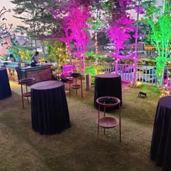 A practical setup for a cocktail party on a lawn, featuring standing cocktail tables with black covers and a fully equipped bar counter in the background, all under festive lighting.