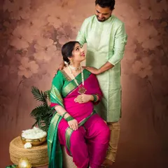 A sweet moment between an expecting couple dressed in traditional Indian clothing. The warm, painterly backdrop complements the vibrant colors of the saree.