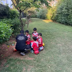 A small group of players sits on their footballs, listening attentively to their coach. This demonstrates the respect and focus we cultivate in our sessions.
