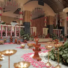 A wide view of a traditional ceremony space we designed. The floor is decorated with scattered flower petals, and the area is filled with terracotta decor, brass urlis, and hanging floral arrangements.