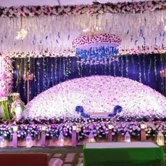 A lavish reception stage completely covered in a dome of white and purple flowers, with a dramatic floral chandelier.