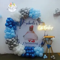 An elegant decoration for a Christening or Baptism celebration. This setup features a custom backdrop with the baby's photo, framed by a blue, white, and silver balloon arch.