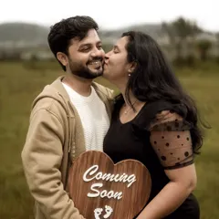 A joyful and candid moment. The mom-to-be gives a happy kiss on the cheek while they both hold a heart-shaped "Coming Soon" sign, perfectly capturing the excitement of this new chapter.