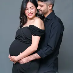 A classic and elegant studio maternity portrait. The couple dressed in all black against a simple grey background creates a sophisticated and timeless look that focuses on emotion.