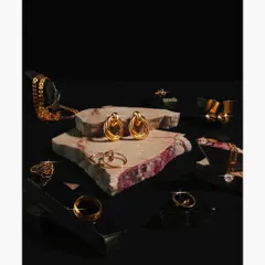 A collection of gold jewelry, including rings and earrings, artfully arranged on pieces of raw marble. The dark, moody lighting and contrasting textures create a luxurious and high-end feel for a brand catalog.