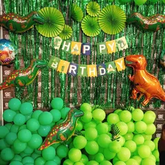 A fun dinosaur themed birthday setup. This decoration features a green shimmer backdrop, various shades of green balloons, and large dinosaur foil balloons to create a prehistoric party atmosphere.