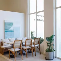 A bright and airy cafe space featuring my cane-back dining chairs and a custom-built upholstered bench. The light wood and neutral fabrics create a calm and inviting atmosphere for customers.