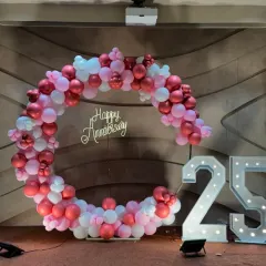 A circular balloon arch in shades of pink and white for a 25th-anniversary party, complete with marquee numbers.