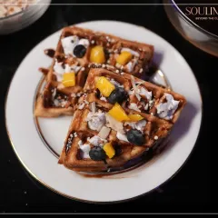 Freshly made waffles topped with mango, blueberries, and a drizzle of chocolate sauce. A delightful and indulgent dessert option for any celebration.