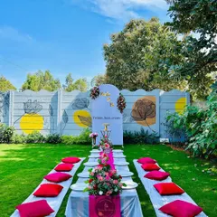 We arranged this lovely outdoor picnic-style bridal shower. The setup includes low seating with bright pink cushions on the lawn, a floral table runner, and a personalized backdrop against a cool mural wall.
