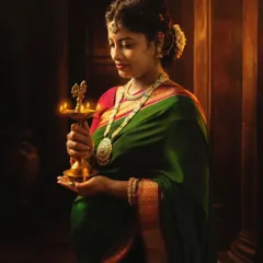 A beautifully lit portrait of a mom-to-be in a traditional green and pink saree, holding a brass lamp (diya) that symbolizes light and life.