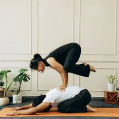 Trust is the foundation. One partner provides a stable base in Balasana (Child's Pose) while the other takes flight in Bakasana (Crow Pose), demonstrating a beautiful fusion of grounding and lifting.