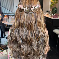 A romantic half-up, half-down style with a braided crown. Tiny pink and white flowers are woven into the braid, adding a delicate and whimsical touch.