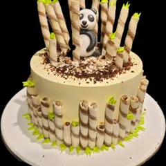 An adorable panda cake set in a bamboo forest made of wafer rolls. This creative design features a cute fondant panda peeking out, making it a delightful and delicious centerpiece.