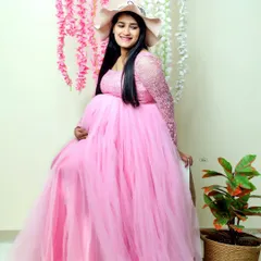 A lovely studio portrait of a mother-to-be in a flowing pink tulle gown. The floral backdrop and soft lighting create a cheerful and feminine atmosphere.