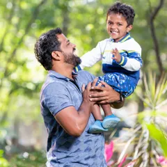 A father lifts his son up, both sharing a moment of pure joy and laughter. This candid outdoor shot perfectly captures the special bond between a dad and his child.