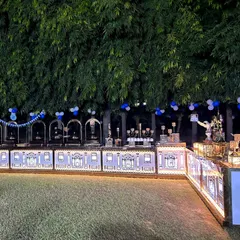 An expansive view of our beautifully lit catering counter at an outdoor evening event. The intricate design on the counter facade, combined with the lush green backdrop, creates a truly magical setting.