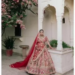 A classic bridal portrait set against the iconic arches and bougainvillea of a Jaipur palace. The vibrant red lehenga contrasts beautifully with the timeless architecture.