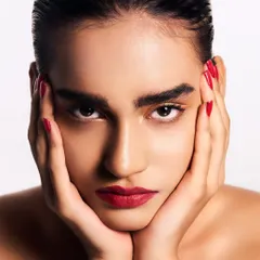 Here, the focus is on the intensity of the gaze, framed by bold brows and complemented by a rich, matte red lip. The sleek hair and matching red nails complete this powerful and cohesive beauty statement.