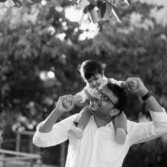 A joyful black and white photo celebrating fatherhood. The happiness on both the father's and son's faces is palpable in this classic outdoor portrait.