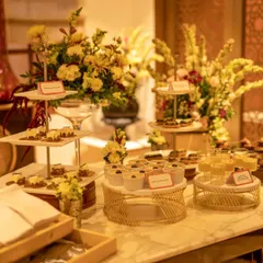 A gorgeous Diwali-themed dessert table. The spread features an array of Indian fusion sweets, including Gulab Jamun Cheesecake and Saffron & Pistachio Panna Cotta, all beautifully arranged with fresh flowers.