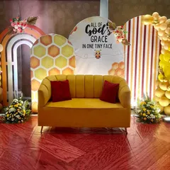 This is a sweet "bee-themed" backdrop I created for a naming ceremony. It features multiple arched panels with honeycomb patterns and stripes, framed by a yellow and peach balloon garland. The comfy yellow sofa is perfect for photos.