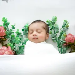 A touch of greenery adds a fresh, natural feel to this minimalist setup. The baby is wrapped in white, lying on a clean white surface.