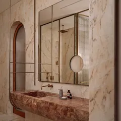 A closer view of the red marble vanity, showing its seamless, curved form and the elegant brass fixtures. The entire space is clad in a richly veined beige marble.