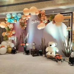 For a modern, bohemian-style baby shower, we paired a teddy bear theme with natural elements like pampas grass. The organic balloon garland in peach, blue, and white complements the arched backdrops and "Oh Baby" sign.