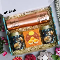 A luxurious Diwali gift box featuring a hammered copper bottle, two decorative tins for sweets or dry fruits, and a box of motichoor ladoo. The set is completed with festive diyas for the occasion.