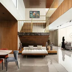 Inside Villa Shakthi in Kerala, a double-height volume connects the dining and family areas. The staircase is a sculptural element, transitioning from marble to wood and steel, creating a dramatic focal point that anchors the home's social core. This view highlights our integrated approach to interior architecture and material expression.