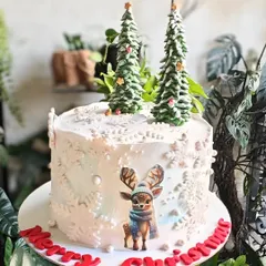 A whimsical white Christmas cake decorated with edible snowflakes, cute reindeer, and fondant Christmas trees. A perfect centerpiece for your holiday table.