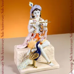 A serene depiction of Lord Krishna playing his flute, accompanied by a peacock. This porcelain idol, with its gentle colors and gold accents, captures a moment of divine playfulness and peace for your sacred corner.