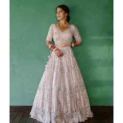 A full-length portrait of a bride in her magnificent lehenga. The intricate details of her outfit and her graceful pose against a simple green background create a stunning image of bridal elegance.
