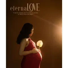 "eternaLOVE." This stylized studio portrait uses dramatic lighting to highlight the baby bump. The mother-to-be, in a striking red dress, holds a single flower, symbolizing the new life and eternal love that is beginning.