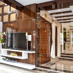 For this grand living room, I designed a floor-to-ceiling entertainment wall using high-gloss wood laminate, complemented by a white asymmetrical shelving unit. The use of marble flooring and intricate ceiling details enhances the sense of luxury and scale in this duplex home.